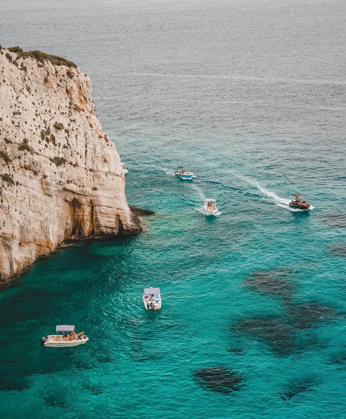 Boats drifting beside the white Zakynthos cliffs